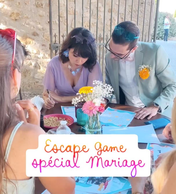 Des invités en tenue de mariage, dont les mariés, penchés sur les feuilles d'énigmes de l'escape game autour d'une table dressée en extérieur, fleurs et cartes de jeu étalées devant eux