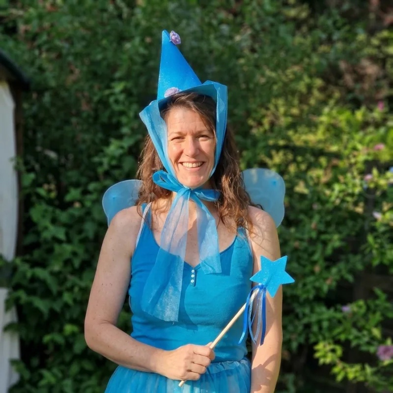 Claire Lys costumée en marraine la bonne fée, chapeau, ailes et baguette étoilée, tout sourire dans un jardin